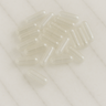 A small pile of empty, transparent size "0" vegan capsules scattered on a smooth white marble surface.