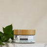 A jar of Megan & Co. Adaptogen Boost Herbal Powder placed on a white surface with a green leafy herb in the background.