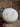 A single round, white bath bomb sprinkled with dried purple lavender buds, resting on a rustic stone surface with a sprig of fresh lavender in the background.