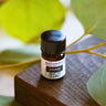 A small bottle labeled 'AWAKE' with essential oil, placed on a wooden surface surrounded by green leaves.