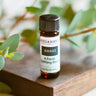 A small bottle labeled 'AWAKE' with a description of 'A Fresh Awakening Blend' placed on a wooden surface with green leaves in the background.