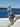 Person holding a glass bottle with a bamboo cap by a body of water