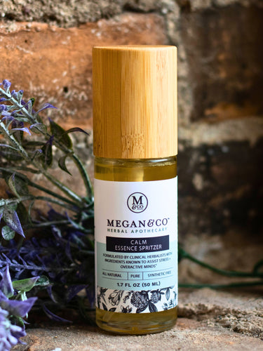 Bottle of Megan & Co Calm Essence Spritzer with a wooden cap on a stone surface with lavender.
