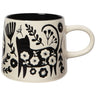 A 14 oz cream-colored stoneware mug featuring a black silhouette of a cat adorned with white flowers, surrounded by various botanical imprints.