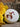 A single round, white bath bomb topped with vibrant dried rose and orange botanical petals, resting on a rustic stone surface next to a bright yellow flower.