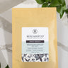 Packaging of 'Daily Boost, Tea Blend' by MEGAN & CO., with a label and loose-leaf tea inside, placed on a marble surface with leaves in the background.