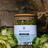 Glass jar with dried herbs labeled 'Megan & Co' on a stone background with green leaves.