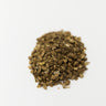 A small mound of dried, chopped brown burdock root pieces centered on a solid white surface.