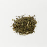 A small, textured mound of dried, dark green comfrey leaves and chopped stems centered on a clean white surface.