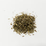 A small, textured mound of dried, sage-green damiana leaves and finely chopped stems centered on a clean white surface.