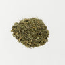 A small, textured mound of dried, forest-green dandelion leaves, cut and sifted, centered on a plain white surface.