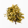 A small mound of dried hawthorn leaves and white flower fragments, featuring various shades of muted olive green and ivory, on a plain white surface.