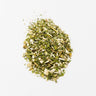 A small mound of dried motherwort leaf, appearing as a mixture of finely chopped green herbal fragments and small white-to-tan woody pieces, staged on a clean white background.
