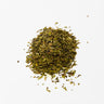 A small mound of dried peppermint leaf, consisting of vibrant green and slightly darker forest-green herbal flakes with occasional small, pale stem pieces, staged on a clean white background.