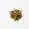 A small mound of dried plantain leaf, consisting of light olive-green herbal flakes and thin, tan stem fragments, staged on a clean white background.
