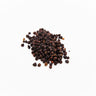 A small mound of dried schisandra berries, showing their characteristic shriveled, dark reddish-purple to black appearance, staged on a clean white background.