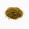 A small mound of dried St. John's Wort aerial parts, featuring a finely textured mix of muted green leaf fragments, thin yellow-tan stems, and dark brownish-orange flower buds, staged on a clean white background.