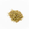 A small mound of dried Uva Ursi leaves, featuring a mix of small, leathery herbal flakes in shades of olive green, tan, and occasional reddish-brown, placed on a clean white background.