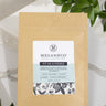A package of 'Fit As A Fiddle' tea blend from Megan & Co. with a label showing the brand name and product name, placed on a surface with a light background and some green leaves.