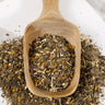 Wooden scoop filled with dried herbs on a white surface