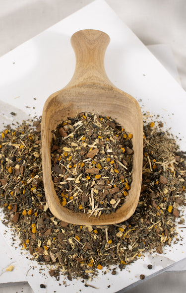 Wooden scoop filled with dried herbs on a white surface