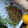 Herbs and a lemon on a white plate with a wooden surface underneath