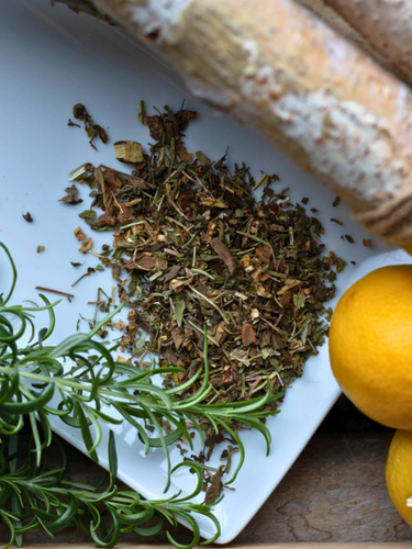 Herbs and a lemon on a white plate with a wooden surface underneath
