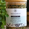 Glass jar of Megan & Co. Honest Tox tea blend with a wooden lid on a blurred natural background.