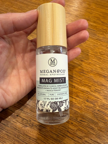 MEGAN & CO. Product, Mag Mist Spray held in hand with wooden background. 