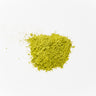 A vibrant, bright-green mound of finely ground Matcha green tea powder with a soft, velvet-like texture, staged on a clean white background.