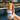 A hand holding the Megan & Co. Boji Bliss spritzer bottle with a wooden cap, staged against a scenic background featuring a Ferris wheel, a wooden bridge, and a glimpse of the sea.