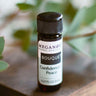 An 8ml amber glass bottle of Megan & Co. Bouquet essential oil blend on a wooden surface, featuring notes of champaca, green tea, and rose absolutes with a blurred leaf background.