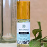 A 50ml glass spritzer bottle of Megan & Co. Bug Ban, staged on a white surface with fresh green leaves and a bottle with measurement markings, formulated with Cedarwood, Lavender, and Geranium.