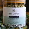 Megan & Co. Chest Re-Leaf tea in a glass apothecary jar with a bamboo lid, surrounded by eucalyptus leaves at the bottom with a soft, blurry background.