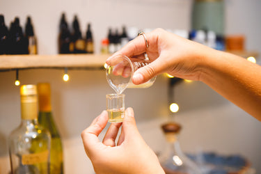 A clinical herbalist measuring essential oils using different sized glass beakers, inside a laboratory workstation.