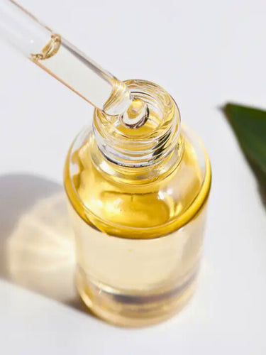 Close-up of a glass dropper along with a designated bottle of an essential oil, with a single golden drop poised to fall, showcasing the oil's thick, clear texture.