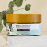 Megan & Co. Heel + Knuckle herbal salve jar with a bamboo lid on a white marble surface with eucalyptus leaves in the background.