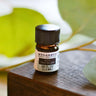 A 2.3ml (5/8th dram) amber glass bottle of Kid's Chest Re-Leaf essential oil on a wooden surface with a blurred leaf background, featuring kid-safe herbs like Lavender, Thyme, and Spearmint.