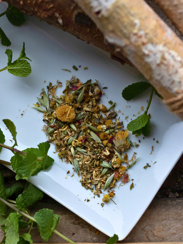 Peaceful Prairie loose leaf tea on a white plate with fresh mint leaves and a natural tree branch, featuring calming herbs like chamomile and linden.