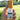 A hand holding the Purify room and body spritzer bottle with a wooden cap against a soft, blurry green grassy nature background.