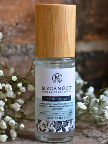 Megan & Co. Sacred Bloom Essence Spritzer with a bamboo cap on a rustic stone surface surrounded by white baby's breath flowers and a brick wall.