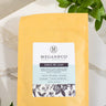 A 1oz sample bag of Megan & Co. Sinus Re-Leaf herbal tea on a marble surface with eucalyptus leaves at the base and a blurred brick wall background.