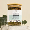 Sinus Re-Leaf tea in a glass jar with a bamboo lid, displayed on a layered marble surface with eucalyptus leaves at the base.