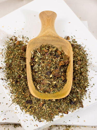 Sinus Re-Leaf loose leaf herbal tea on a wooden scoop, resting on scattered tea blend atop a white layered marble surface.
