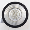A top-down view of a circular stainless steel tea infuser basket lid, featuring a brushed metal finish with concentric light reflections and the "M & CO" logo engraved in the center. The lid is bordered by a black silicone or rubber ring and includes a small metal tab on the left side for easy removal.