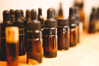 A large batch of clean amber glass essential oil bottles with black dropper caps, organized and ready for filling on a white sterile surface.