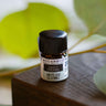 A 2.3ml (5/8th dram) amber glass bottle of Sweet Dreams essential oil on a wooden surface with a blurred leaf background, featuring calming Organic Lavender, Chamomile, and Melissa.
