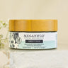 Megan & Co. Sweet Tush herbal salve jar with bamboo lid on white marble with baby's breath flowers on its side.
