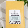 A 1oz sample bag of Megan & Co. Winter Warmer tea on a marble surface, staged with green leaves.