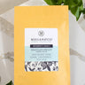A 1oz sample bag of Megan & Co. Women's Daily tea on a marble surface, staged with green leaves.
